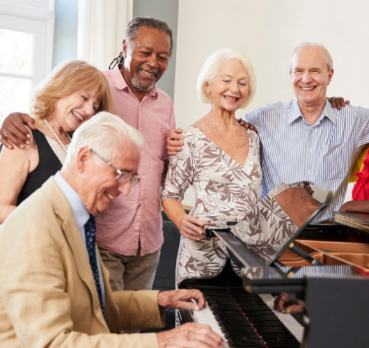 Older man playing the piano while diverse seniors gather around to listen