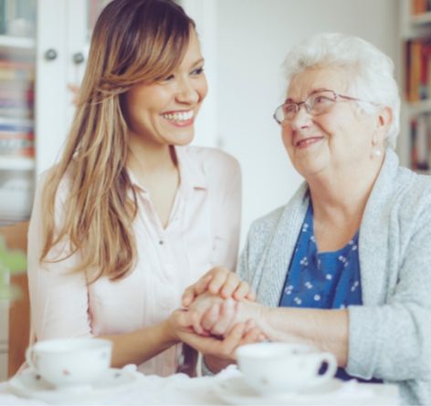 Female volunteer holding elderly woman's hand while having tea together