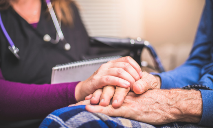 nurse holding the hand of senior with blanket on his lap